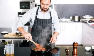 Mężczyzna w fartuchu gotuje na patelni w nowoczesnej kuchni.