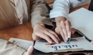 Dłonie analizujące wykresy i tabelę na drewnianym stole.