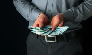 Mężczyzna w szarej koszuli trzyma w dłoniach polskie banknoty 50 i 100 zł.