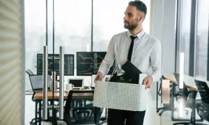 Mężczyzna w białej koszuli i krawacie niesie pudełko z rzeczami z biura.