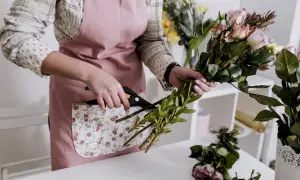 Ręce florystki przycinają zielone gałązki do bukietu róż. Nauka florystyki w praktyce.