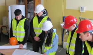 Uczniowie technikum w kamizelkach odblaskowych i kaskach analizują plany, przygotowując się do zdobycia uprawnień budowlanych.