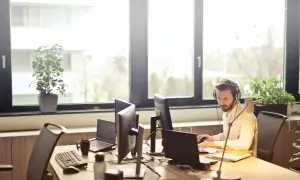 Mężczyzna w słuchawkach pracuje przy komputerze w jasnym biurze.