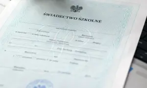 Świadectwo szkolne z orłem i ozdobnymi ramkami, leżące na klawiaturze laptopa.
