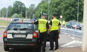 Dwóch funkcjonariuszy Służby Celnej w kamizelkach odblaskowych stoi przy oznakowanym radiowozie.