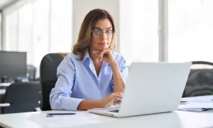 Kobieta w okularach pracuje przy laptopie w jasnym biurze.