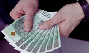 Dłonie trzymające stos banknotów 100-złotowych.