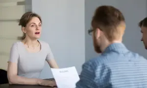 Kobieta podczas rozmowy kwalifikacyjnej, patrząca na rozmówcę trzymającego CV.
