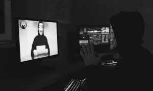 Osoba w masce Guy Fawkesa przed monitorem z podobną postacią i kodem.