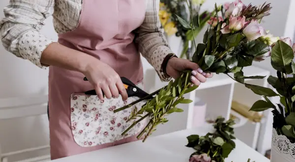 Ręce florystki przycinają zielone gałązki do bukietu róż. Nauka florystyki w praktyce.