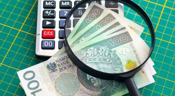Kalkulator, lupa i polskie banknoty 100 zł na zielonym tle.