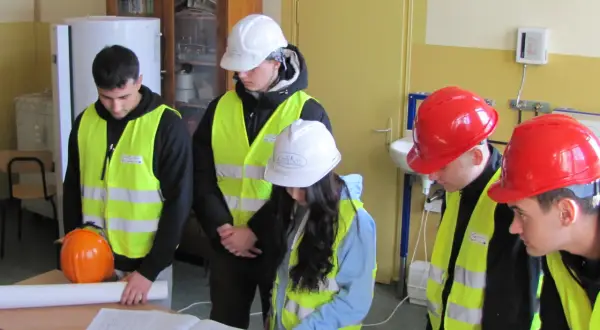 Uczniowie technikum w kamizelkach odblaskowych i kaskach analizują plany, przygotowując się do zdobycia uprawnień budowlanych.