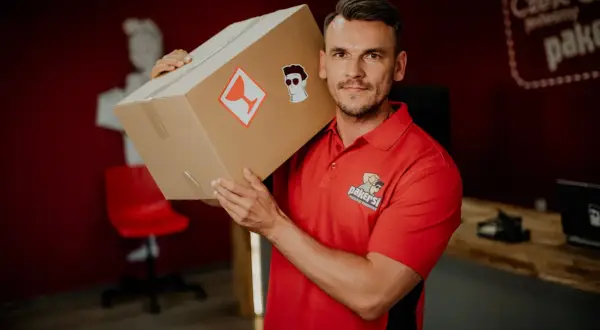 Kurier DPD z paczką na ramieniu. Zastanawiasz się, ile zarabia kurier DPD? Ten pracownik wygląda na zadowolonego z pracy.