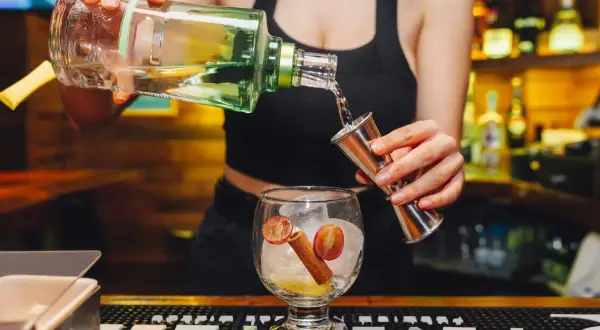 Barman nalewa alkohol z butelki do miarki, przygotowując drinka.