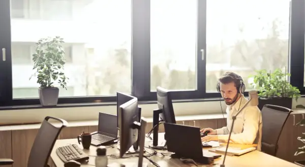 Mężczyzna w słuchawkach pracuje przy komputerze w jasnym biurze.