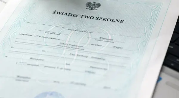 Świadectwo szkolne z orłem i ozdobnymi ramkami, leżące na klawiaturze laptopa.