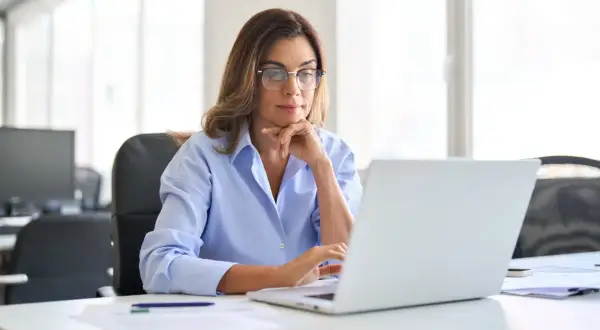 Kobieta w okularach pracuje przy laptopie w jasnym biurze.