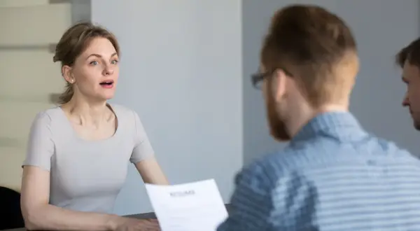 Kobieta podczas rozmowy kwalifikacyjnej, patrząca na rozmówcę trzymającego CV.