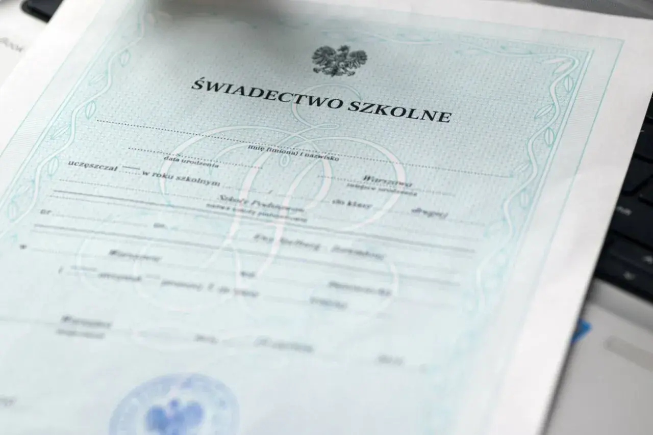 Świadectwo szkolne z orłem i ozdobnymi ramkami, leżące na klawiaturze laptopa.