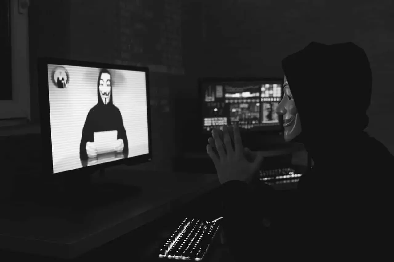Osoba w masce Guy Fawkesa przed monitorem z podobną postacią i kodem.