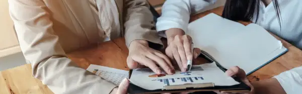Dłonie analizujące wykresy i tabelę na drewnianym stole.