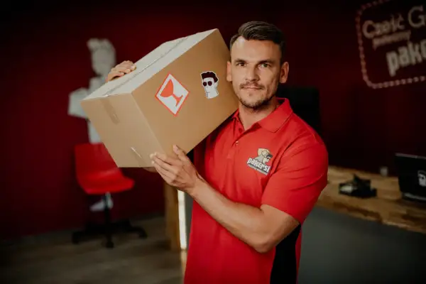 Kurier DPD z paczką na ramieniu. Zastanawiasz się, ile zarabia kurier DPD? Ten pracownik wygląda na zadowolonego z pracy.