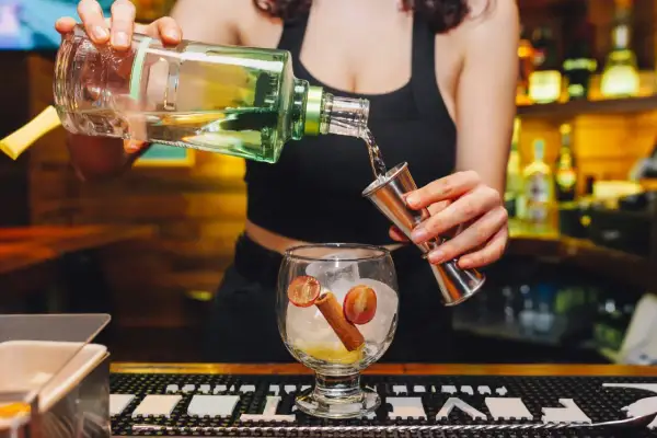 Barman nalewa alkohol z butelki do miarki, przygotowując drinka.