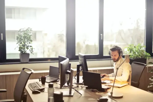 Mężczyzna w słuchawkach pracuje przy komputerze w jasnym biurze.