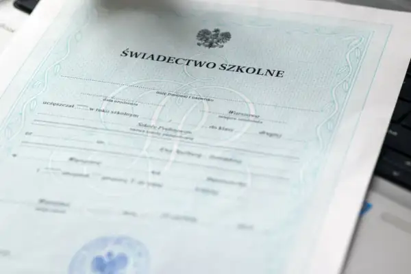 Świadectwo szkolne z orłem i ozdobnymi ramkami, leżące na klawiaturze laptopa.