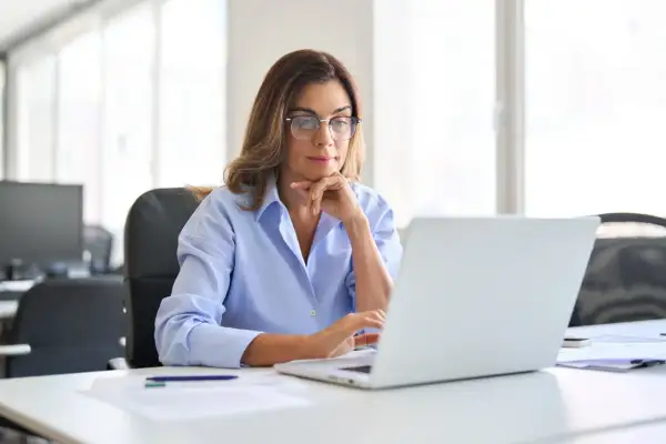 Kobieta w okularach pracuje przy laptopie w jasnym biurze.