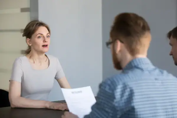 Kobieta podczas rozmowy kwalifikacyjnej, patrząca na rozmówcę trzymającego CV.